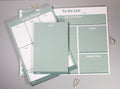 A set of pastel sage green and white stationery items arranged on a light gray surface, including a weekly planner sheet, a to-do list pad, and a notes pad, with small gold decorative cone-like paper clips nearby.